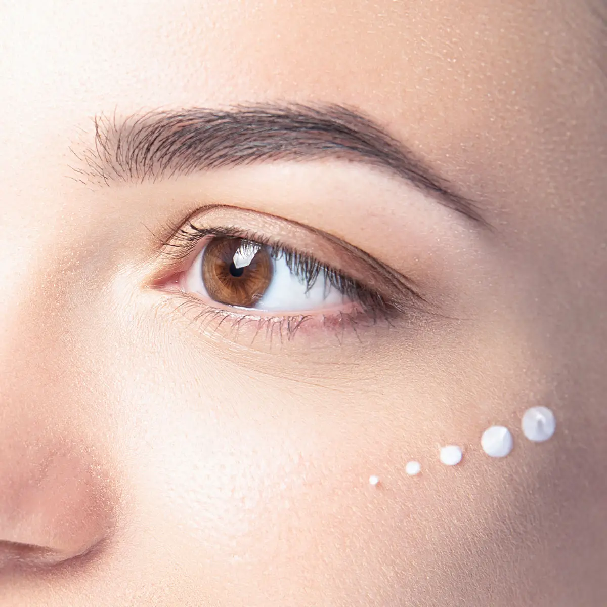 Beautiful model with cosmetic drops of cream on her face on white background close-up.